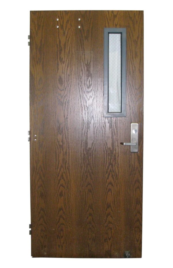 1970s oak school door with one narrow lateral window and original hardware.