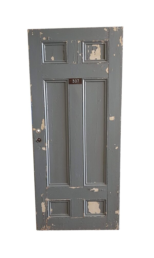 Antique six-panel wood apartment door with a dark gray side, peeling paint, and room number 307 visible near the center.