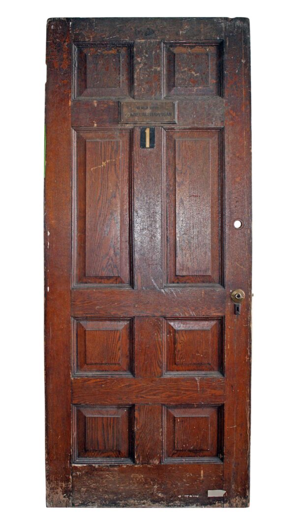 Front view of an antique commercial wood door with eight panels and a dark wood tone, showing a number 1 plaque and a keyhole on the right side.