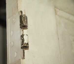 Close-up of a white wooden door showing two original metal hinge leaves along the edge.