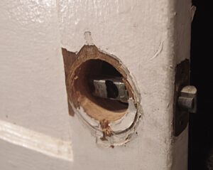 Close-up of a white wooden passage door showing the latch bore and chipped paint around the lock opening.