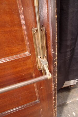Close-up of a medium wood tone commercial door showing the push bar hardware and door edge.