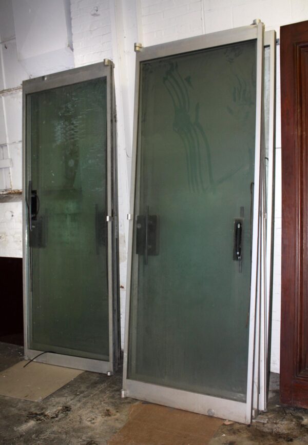 Pair of reclaimed glass entry doors with brushed aluminum frames and streamlined pulls, shown standing upright at a slight angle.