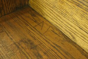 Close-up of the oak bench showing the seat and backrest corner with visible surface wear and a hand-drawn marking.