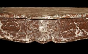 Close-up of a French Louis XV marble mantel with a carved serpentine apron and floral center detail.