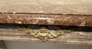 Close-up of a marble mantel frieze with an antique bronze applique centered beneath the shelf.