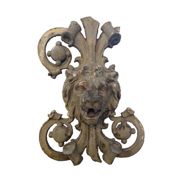 Gray cast iron lion crest with ornate scrollwork and a broken piece on the right side.