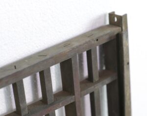 Close-up of an antique bronze bank teller door showing the top edge and hinge bracket with slotted openings and visible wear.