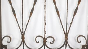 Wrought iron panel with curled scrollwork and vertical bars, shown in close-up with visible age-related rust and a solid frame edge.