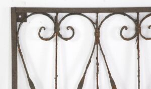 Wrought iron panel with curled scrollwork and a solid frame, shown in close-up with visible rust.