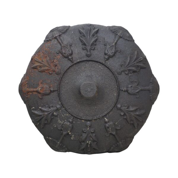 Hexagonal cast iron post finial top with raised leaf motifs, a central round opening, and visible rust on one side.
