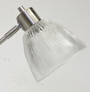 Close-up of a brushed nickel desk lamp with a clear prism glass shade and adjustable metal arm.