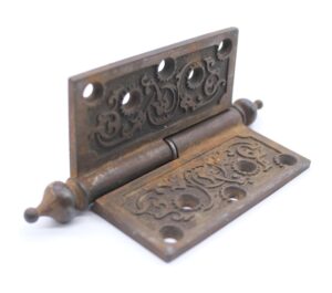 Victorian cast iron butt door hinge with steeple tips, ornate cutouts, and a staggered hole pattern shown in a close-up view.