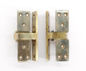 Pair of traditional pocketed pivot door hinges in polished brass, shown as a matching pair with visible screw holes and side profiles.