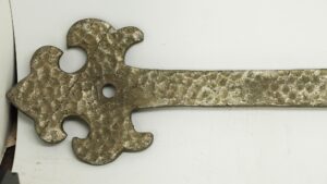 Close-up of a 24-inch door strap hinge with a hammered antique finish and decorative cutouts at one end.