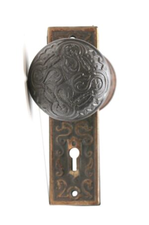 Antique cast iron door knob set with a keyhole back plate, shown in close-up with an ornate round knob and decorative rectangular escutcheon.