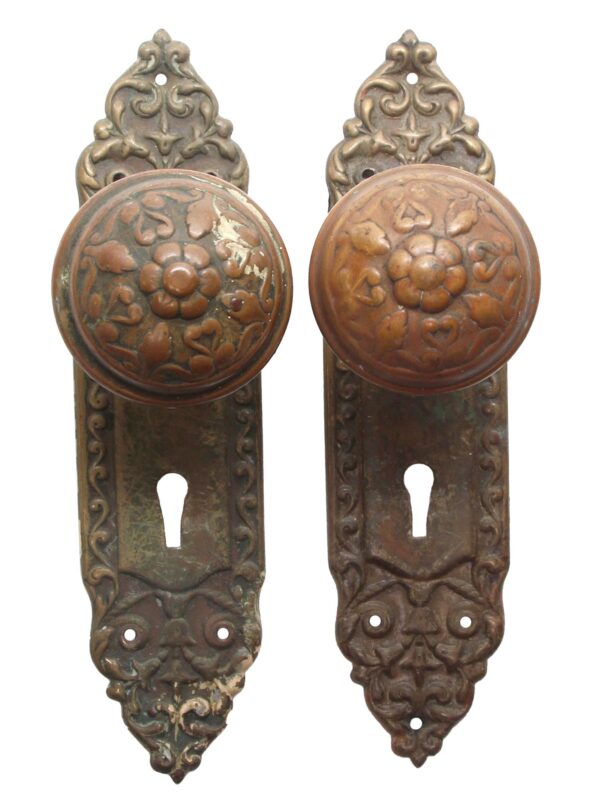 Pair of antique brass door knobs with ornate Victorian back plates and keyhole cutouts, shown side by side on a white background.