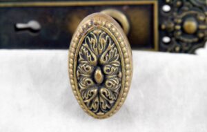 Close-up of an antique bronze oval door knob with an ornate Louis XVI floral pattern.