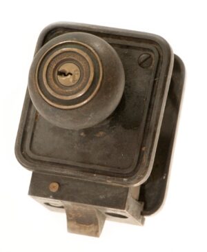 Close-up of an Art Deco cast bronze door lock and knob set with an attached keyed lock and rectangular back plate.