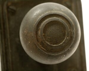 Close-up of a cast bronze door knob showing the round face and worn antique bronze finish.