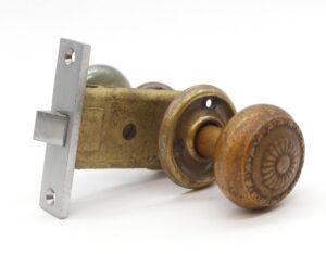 A passage door knob set with one brass patina knob and rosette and a matching nickel plated mortise plate shown in close-up.