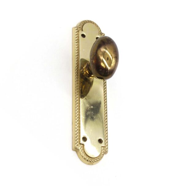 Traditional polished brass dummy door knob set with an oval knob and decorative backplate shown from the front.