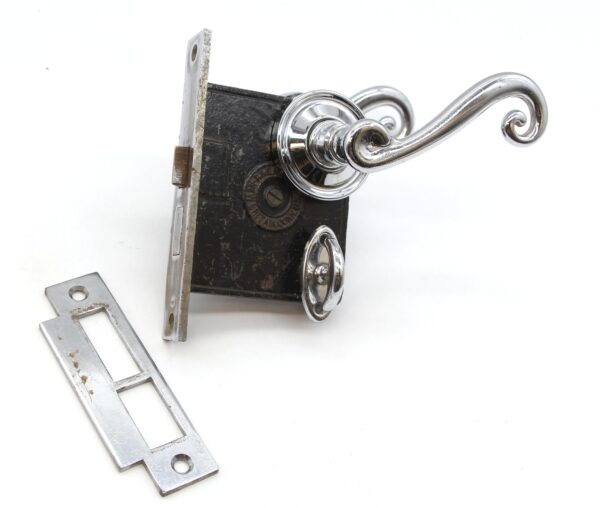 Vintage privacy door lever set with chrome rosettes and swirl lever, shown with the mortise lock and strike plate, displaying surface wear from prior use.