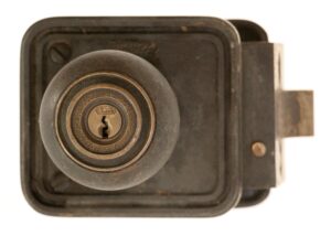 Close-up of an antique bronze door lock with a round knob and keyhole, shown from the front with the latch bolt extending to the right.
