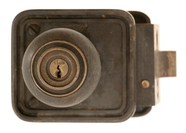 Close-up of an antique bronze door lock with a round knob and keyhole, shown from the front with the latch bolt extending to the right.
