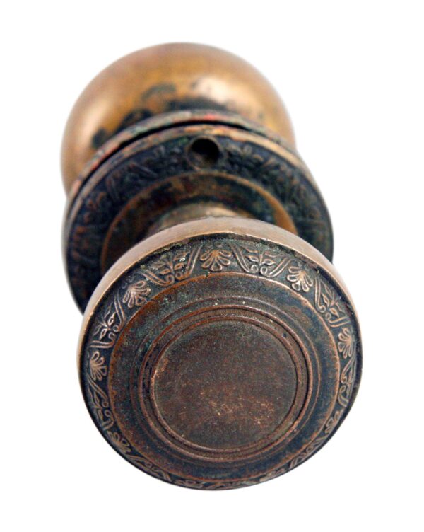 Close-up of an antique brass door knob set showing the round knob face with concentric rings and a floral border pattern.