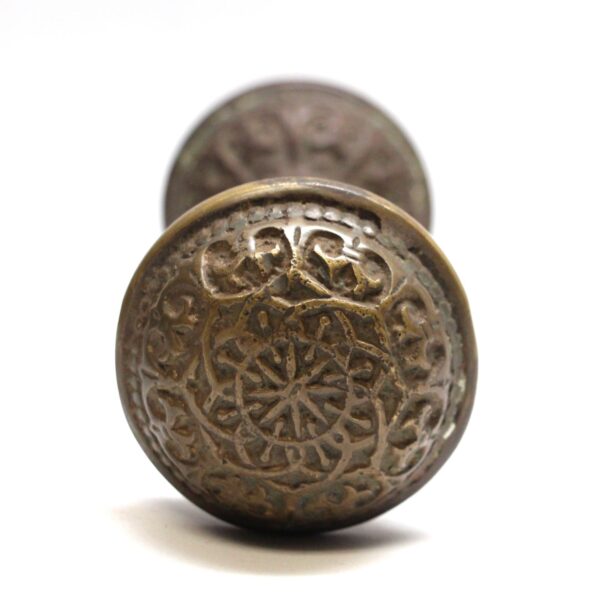 Antique bronze door knob with an eightfold floral pattern shown in a front view.