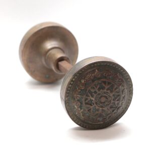 Pair of antique bronze passage door knobs with a spindle, shown in front and back views, one face featuring an eightfold ornamental pattern.