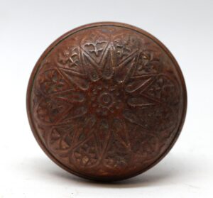 Antique bronze door knob with a radial floral pattern and rounded face.