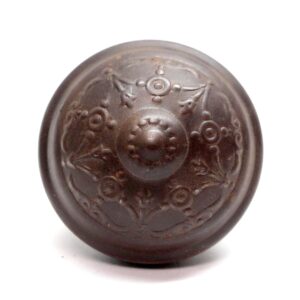 Antique cast iron passage door knob with a raised floral pattern and worn finish.