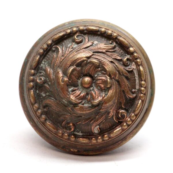 Antique bronze Romanesque door knob with a raised swirl and floral center design shown from the front.
