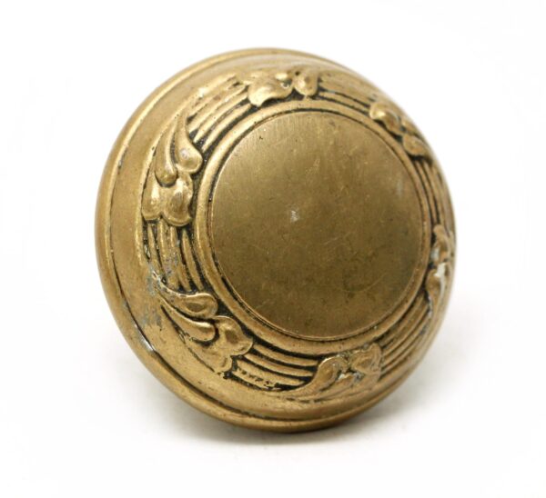 Antique brass door knob with a concentric Victorian floral border, shown front view with visible surface wear.