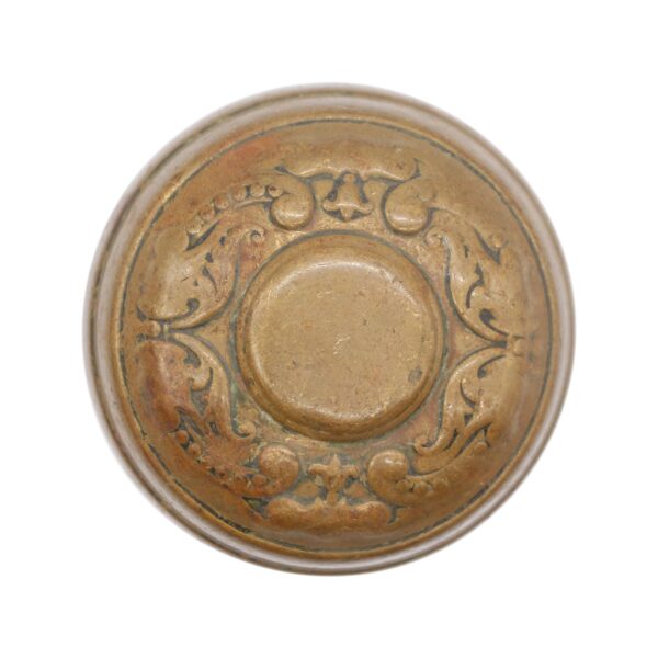 Top view of an antique brass door knob with ornate Flemish scrollwork and a raised center.