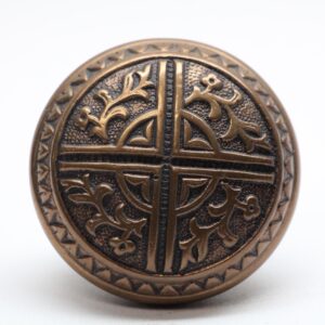 Antique bronze door knob with a round face, raised four-fold floral pattern, and textured outer border shown in close-up.
