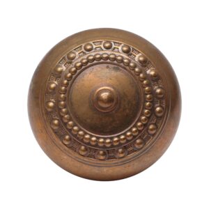 Antique brass door knob with concentric beaded rings and a raised center dome, shown front view.