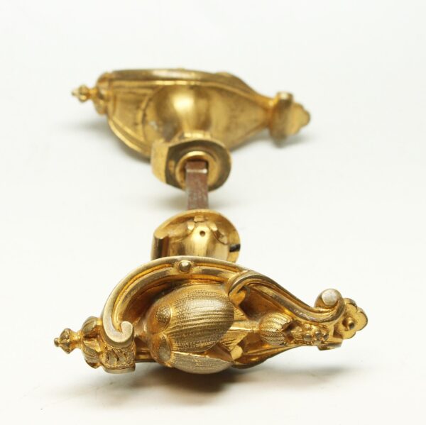 Pair of gilded bronze oval door knobs with a spindle, shown from a close-up angle.
