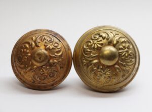 Pair of antique brass Colonial door knobs with ornate floral detailing and domed centers, shown side by side.