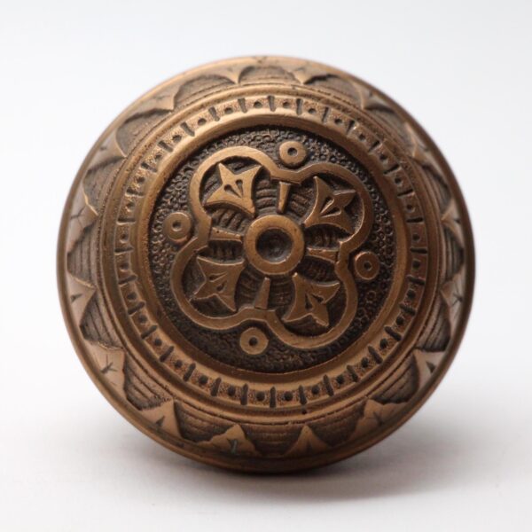 Antique bronze door knob with a fourfold floral pattern and a round rosette design shown in close-up view.
