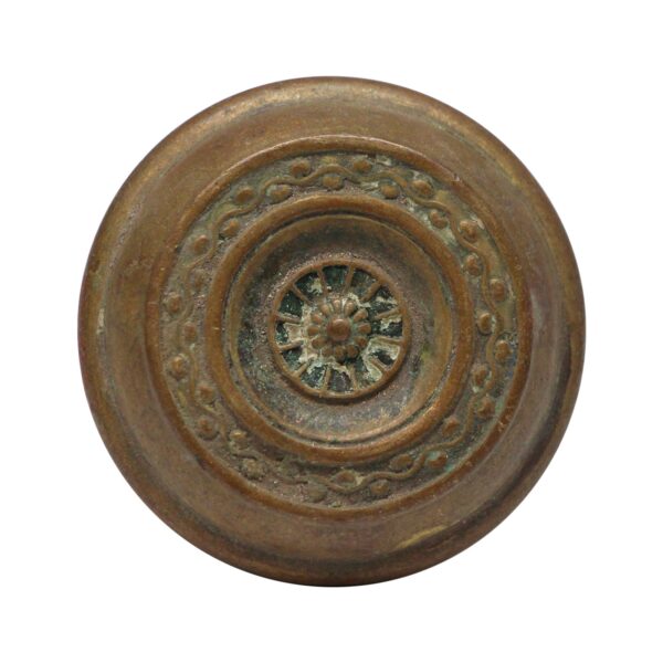 Antique brass passage door knob with concentric rings and a floral center medallion.