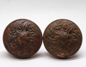 Pair of antique cast iron door knobs with an embossed swirl pattern and visible surface wear, shown side by side.