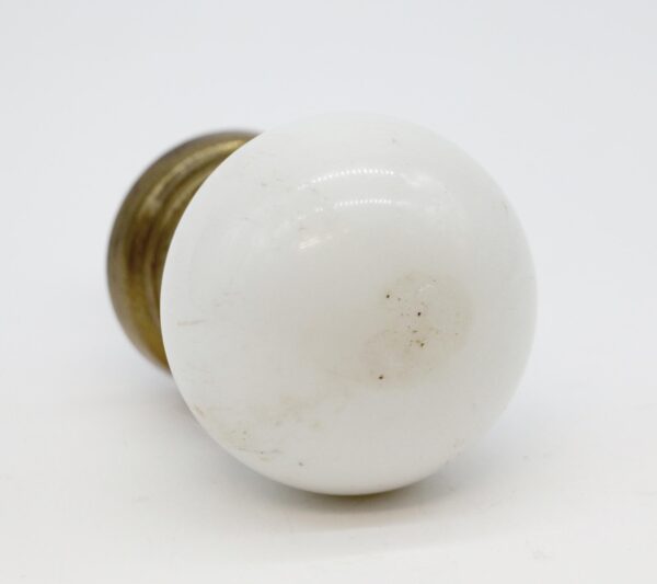 White ceramic ball-shaped door knob with a wide antique brass shank, shown in close-up with visible surface scratching.