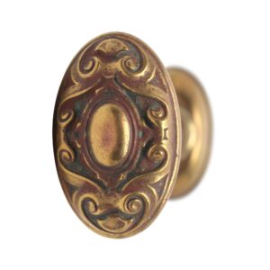 Antique bronze oval door knob with ornate scroll detailing and a raised center oval, shown in close-up from the front.