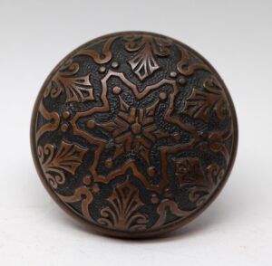 Antique bronze door knob with a raised six-fold star pattern and ornate scroll details.