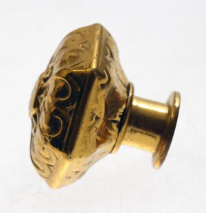 Antique bronze hexagon door knob shown in close-up from the side, with an ornate vernacular design and threaded shaft visible.