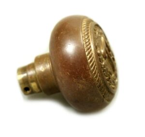 Single antique bronze passage door knob with an emblematic face and engraved border detail, shown in close-up from the side.