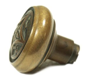 Close-up of an antique bronze Gothic door knob with a four-fold decorative face and worn surface.